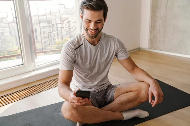 Person at home reviewing their phone while resting on a yoga mat during recovery, preparing for a medical clearance certificate