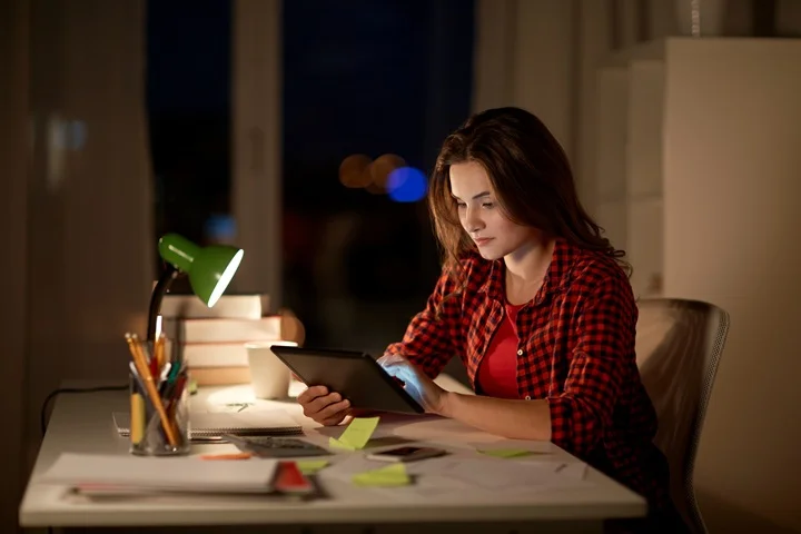 University student checking her phone at a sunlit desk with notebook open, arranging a medical certificate for a missed exam