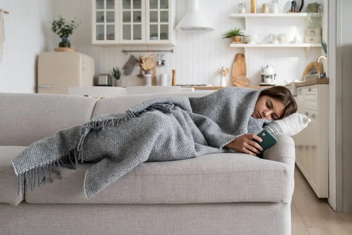 Person resting at home on couch using smartphone to book a sick leave certificate for a common illness through OMC Health