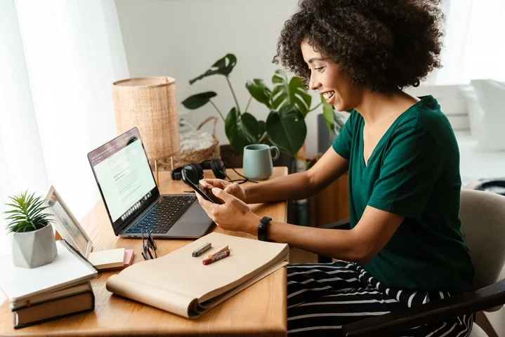 Woman smiling while checking her phone at home desk, arranging a carer's leave certificate consultation