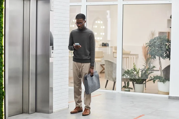 Australian man in smart-casual attire holding his phone and coffee while leaving home in the morning, on his way to return to work after medical clearance