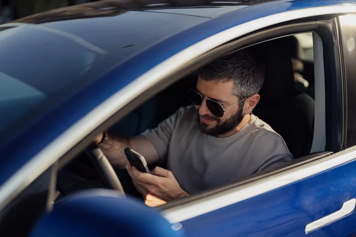 Driver seated in a parked car checking their phone before completing a fitness to drive certificate