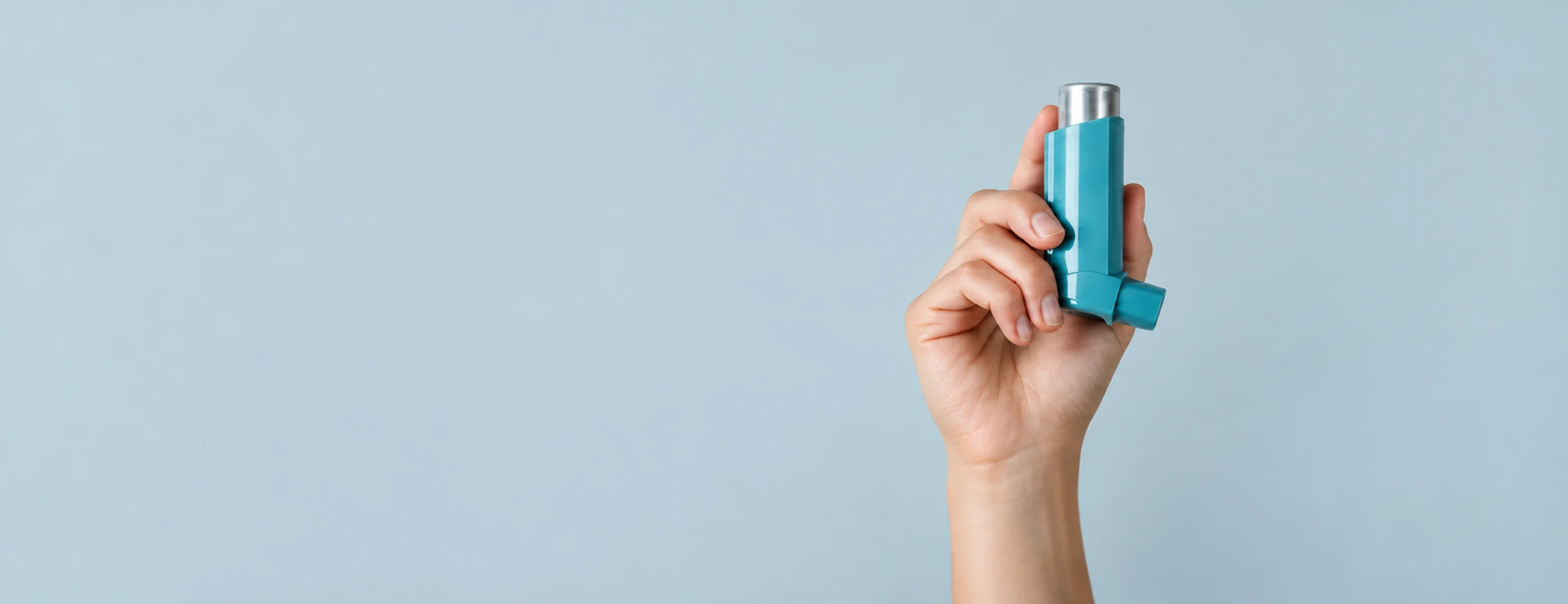 Close-up of a hand holding a reliever inhaler against a plain light background, representing an asthma flare-up