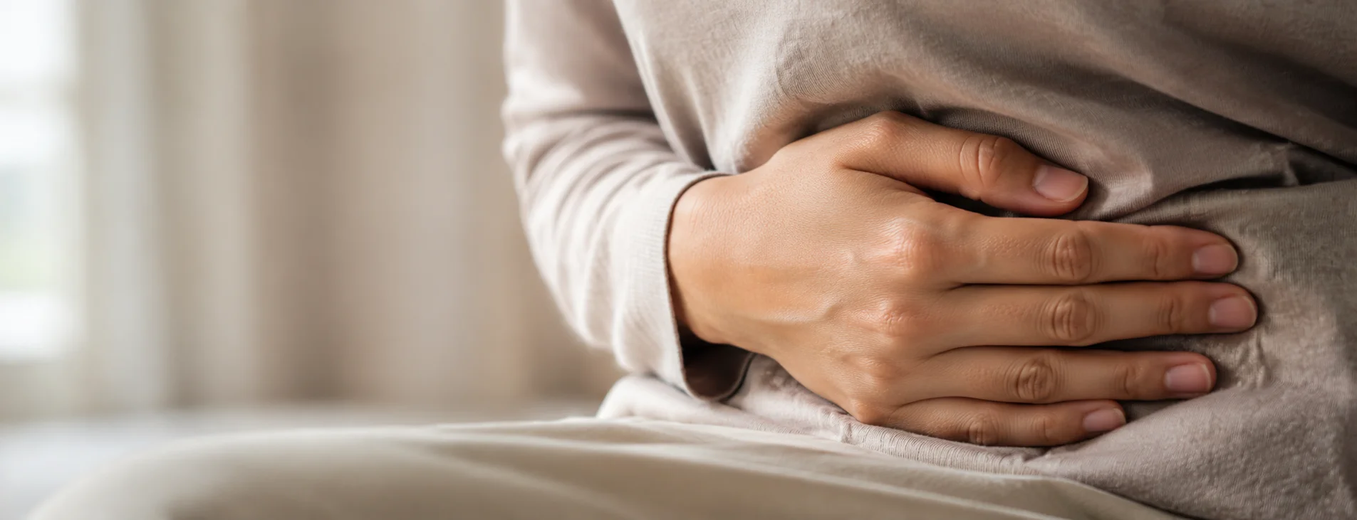 Close-up of a hand resting gently over the abdomen while seated, representing a Crohn's disease flare