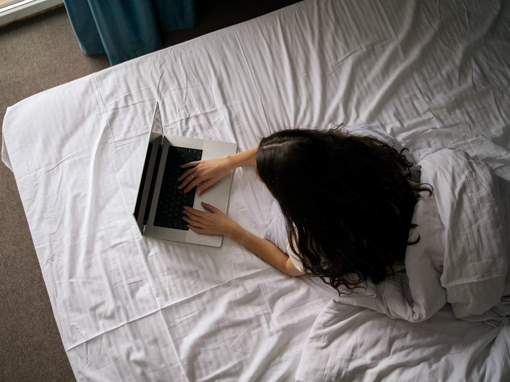 Student lying face down on a bed with an open laptop, unable to keep studying