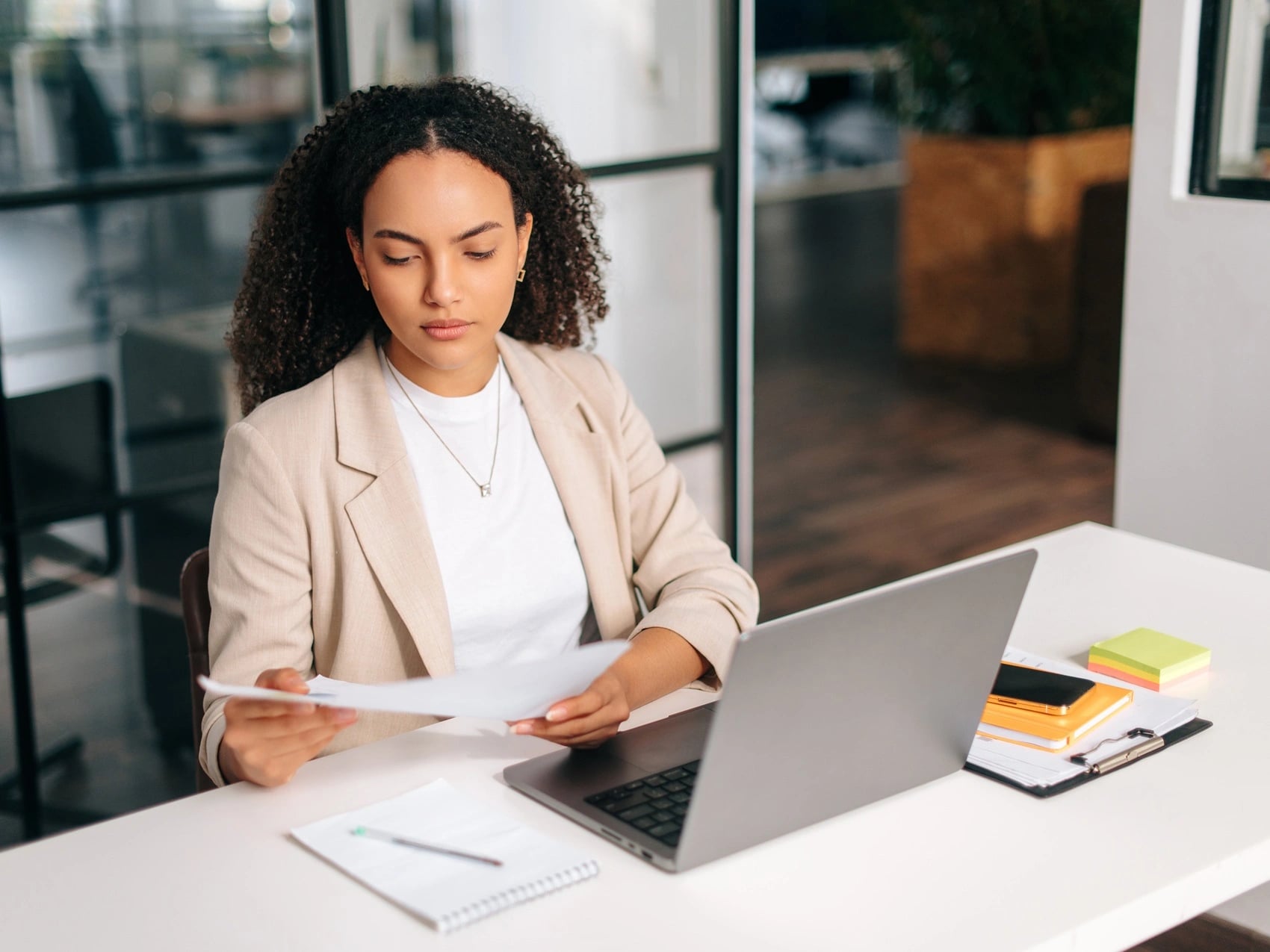 Woman in an office reviewing a printed medical certificate while verifying a medical certificate online on laptop.