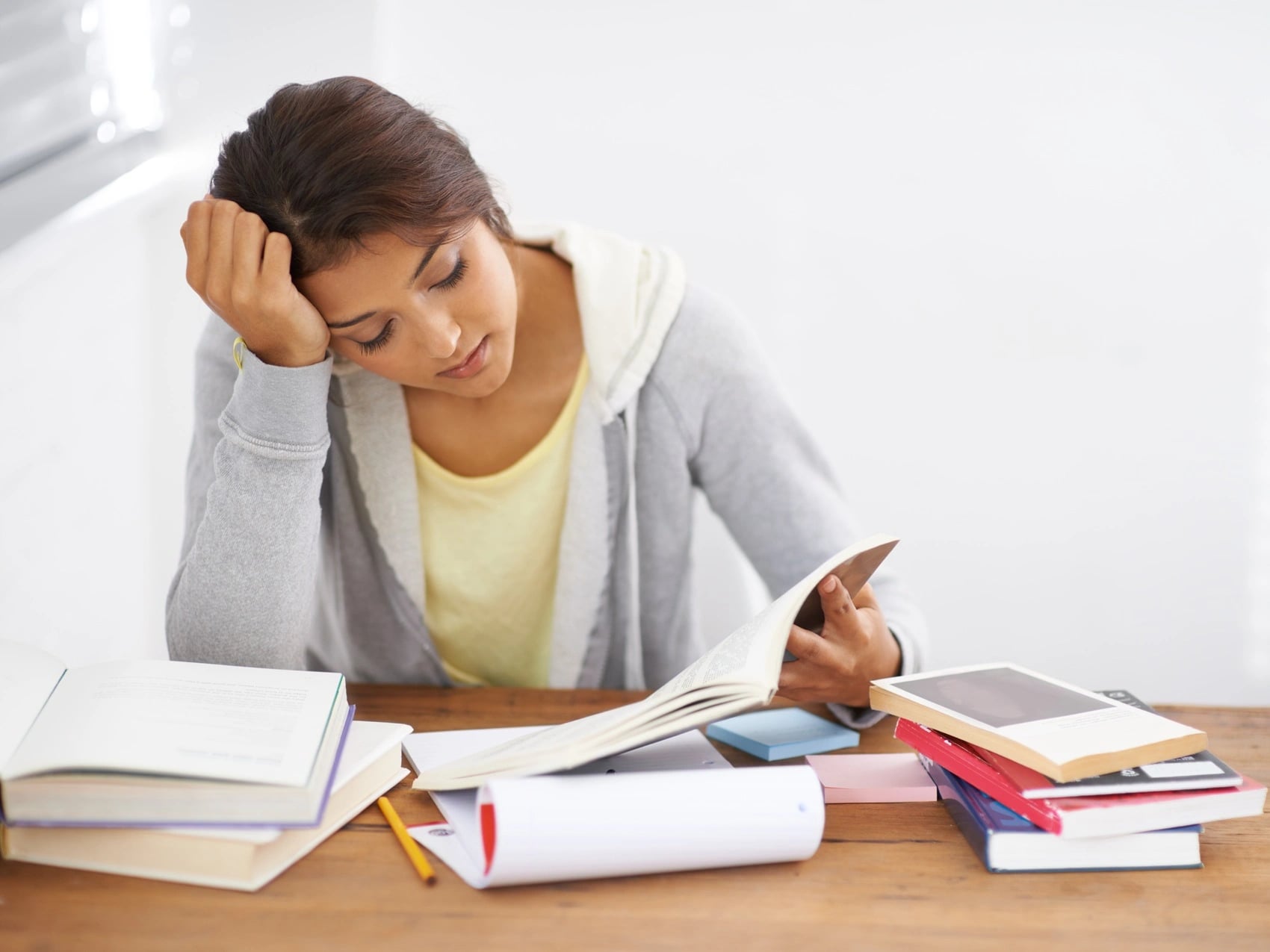 Student at a desk with open textbooks, resting her head on one hand