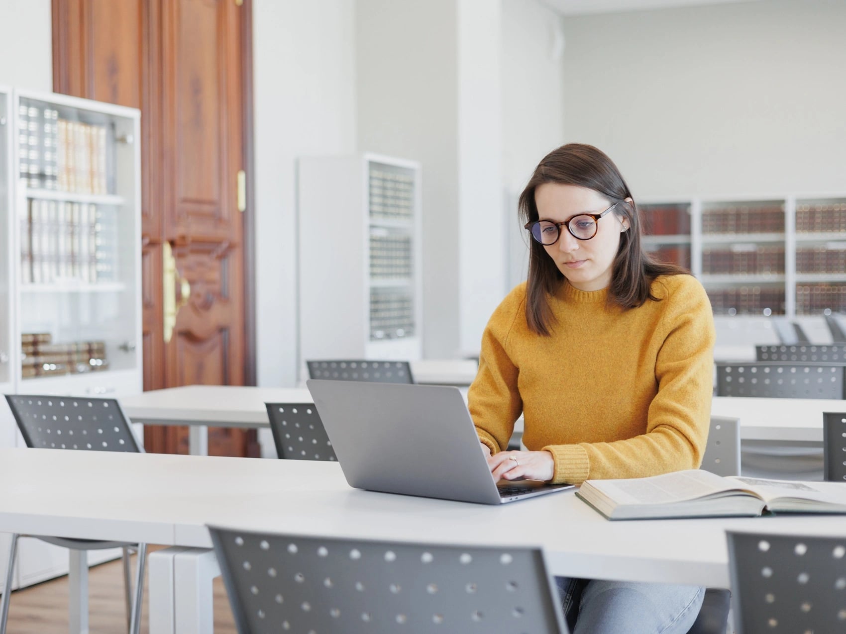 Student working alone at a university library desk with a laptop and open book