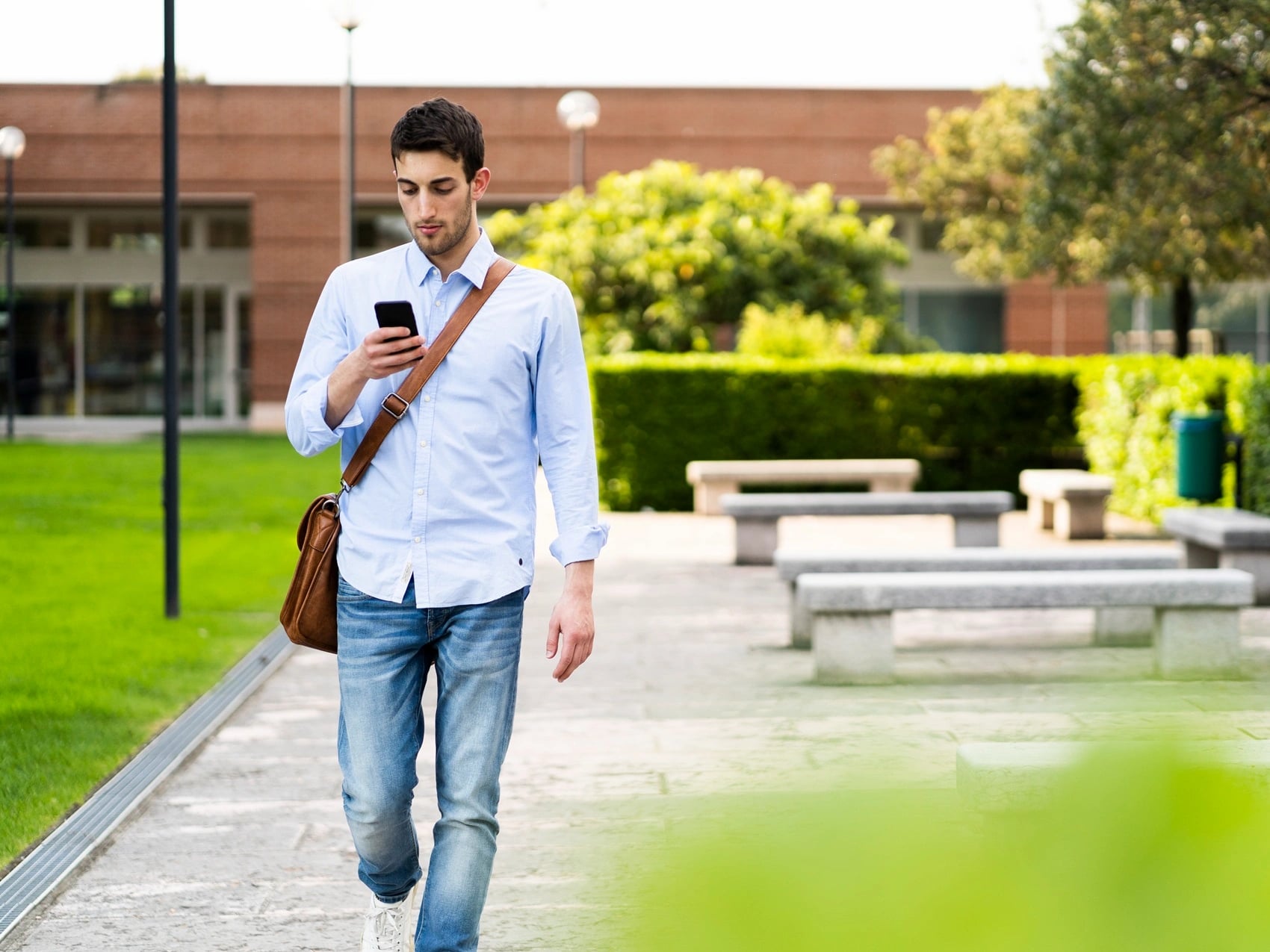 Student walking along a campus path while reading a message on his phone