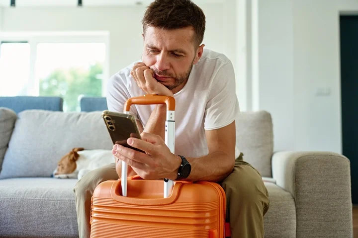 Person sitting beside a packed suitcase reviewing a travel app on their phone before requesting a medical cancellation letter for a travel insurance claim