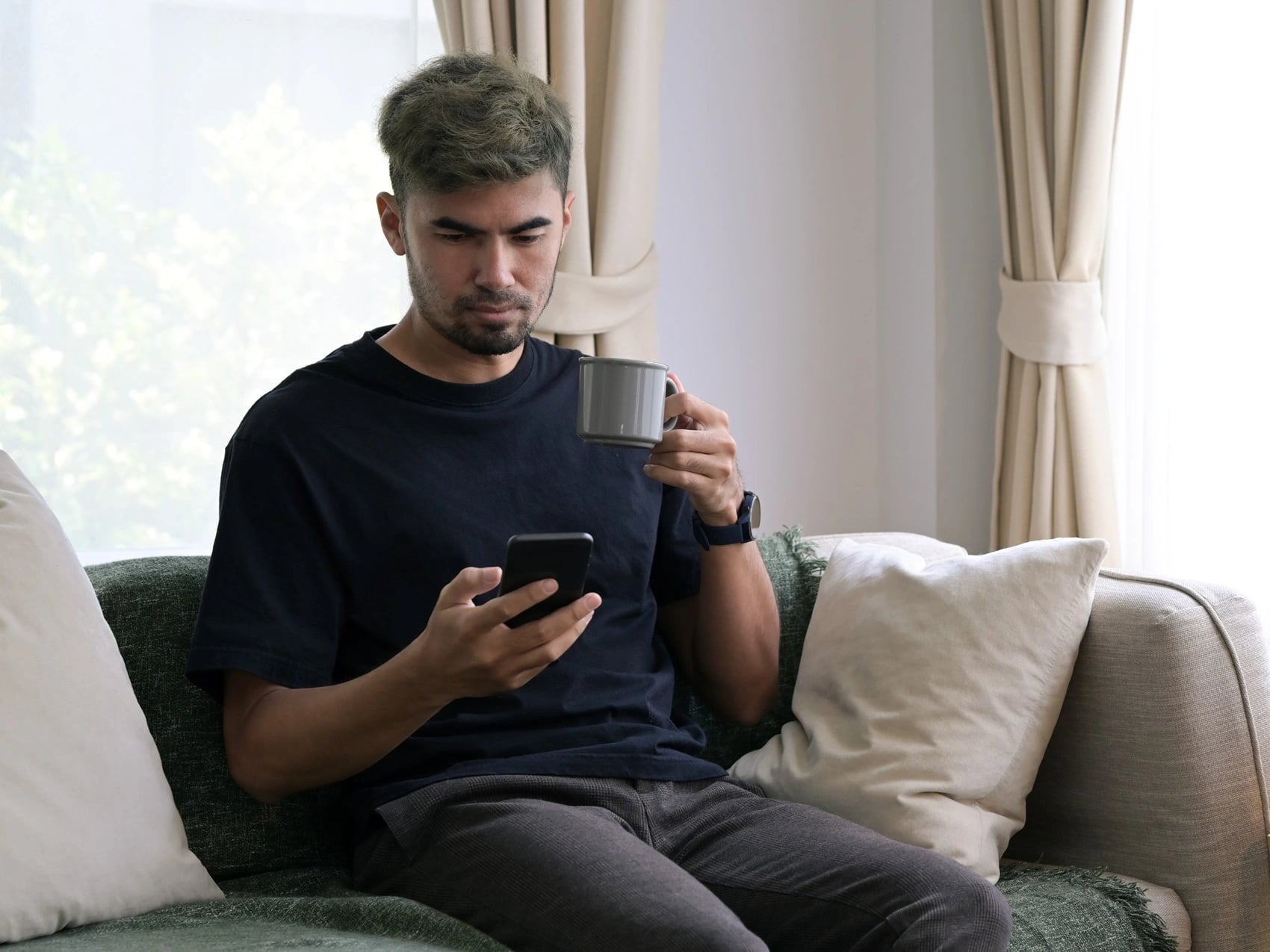 Man on the lounge at home with a coffee and his phone, arranging a weekend medical certificate.