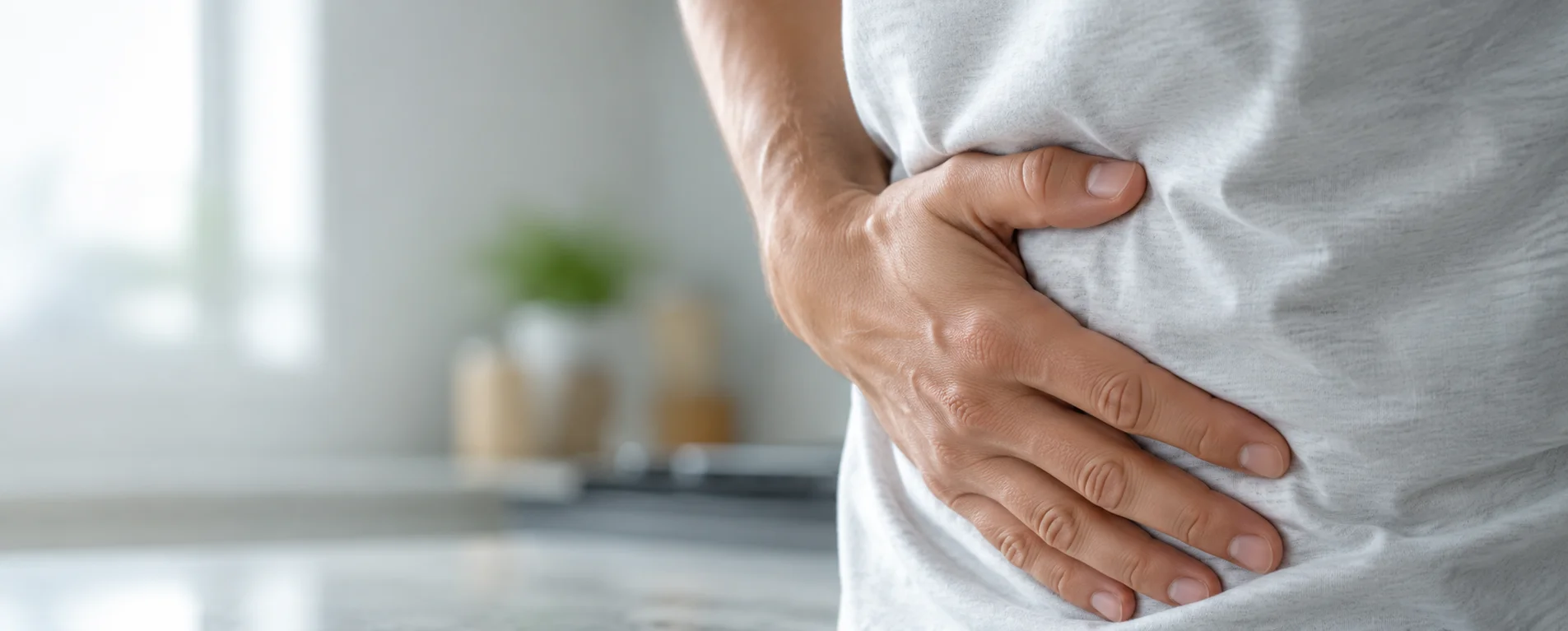Close-up of a hand pressed to the lower abdomen while leaning over a kitchen counter — Sick Leave Certificate for Irritable Bowel from OMC Health