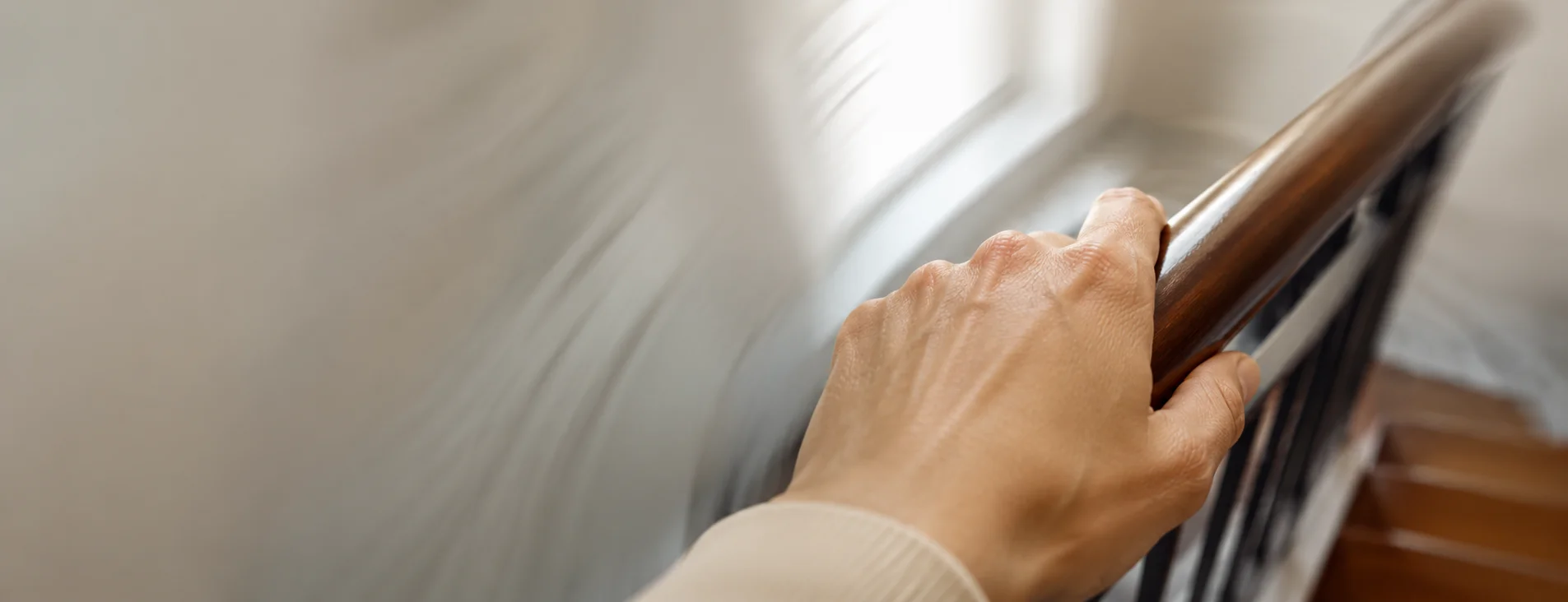Close-up of a hand gripping a stair railing with a blurred, swirling background suggesting disorientation — Sick Leave Certificate for Vertigo from OMC Health
