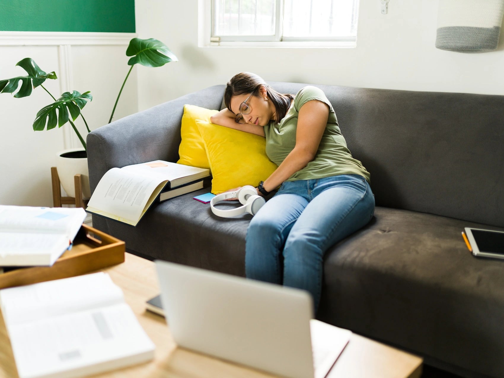 Student asleep on a couch at home with open textbooks and a laptop set aside