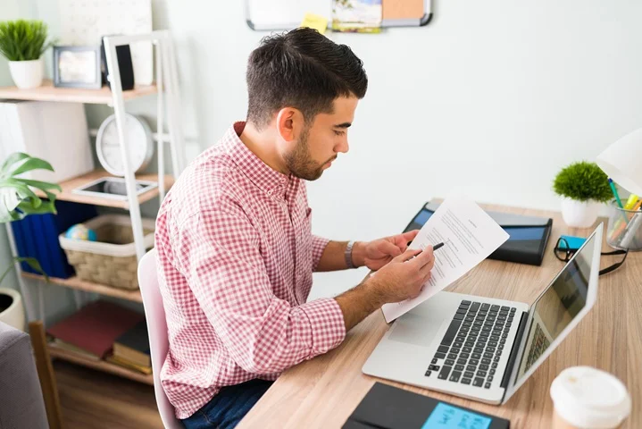 Person reviewing a printed WorkCover Certificate of Capacity from OMC Health alongside a laptop at a home desk