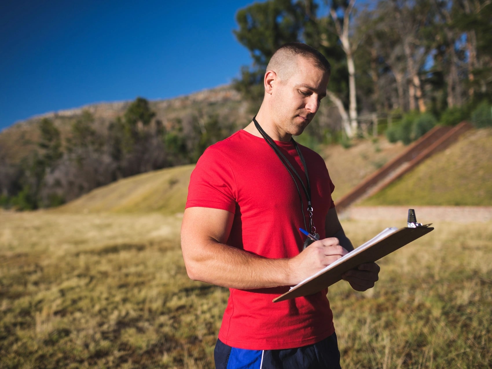 Northern Territory worker in a red shirt completing a form on a clipboard in open dry grassland