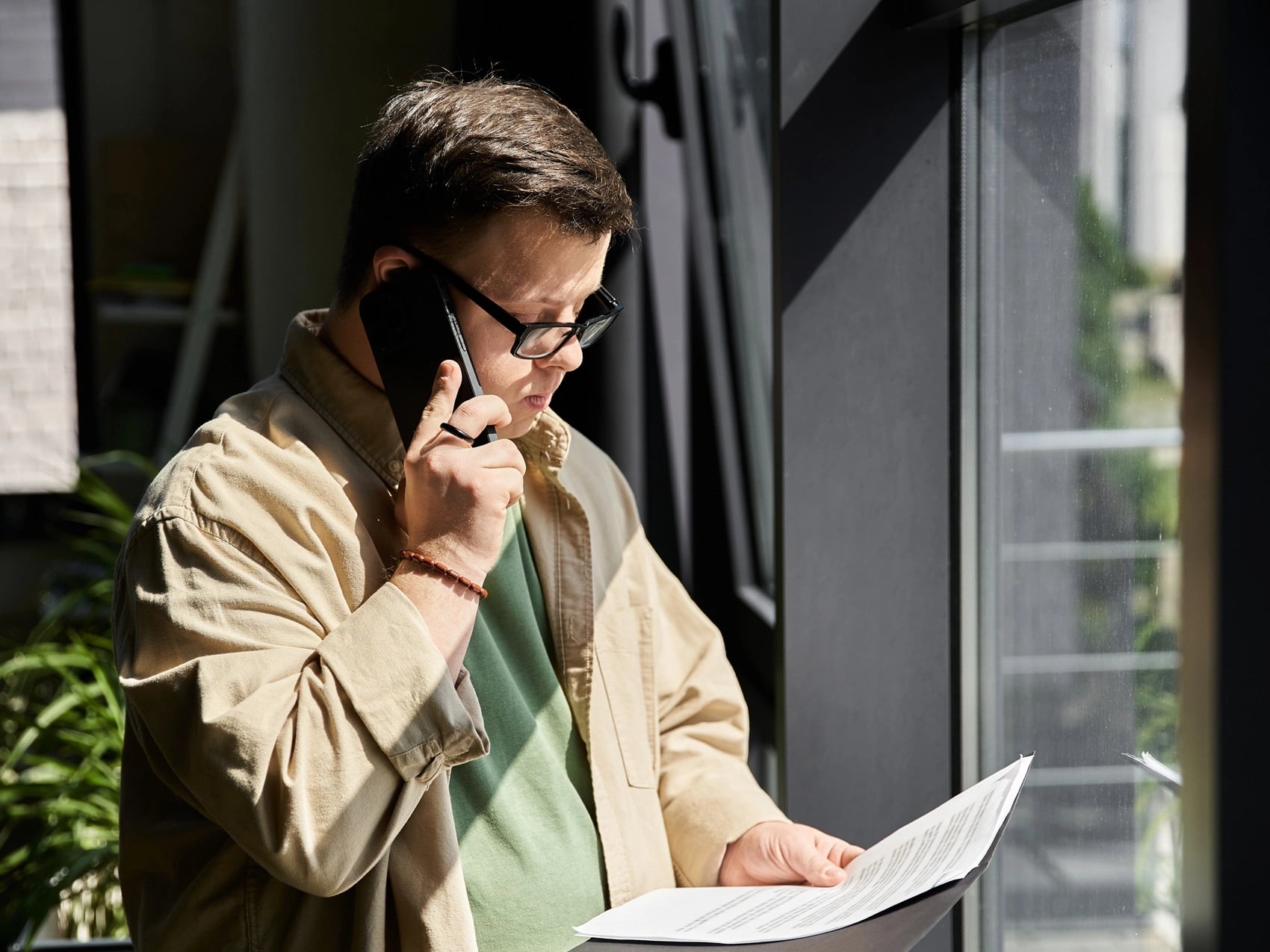 Tasmanian worker in a jacket on a phone call while reading paperwork beside a window